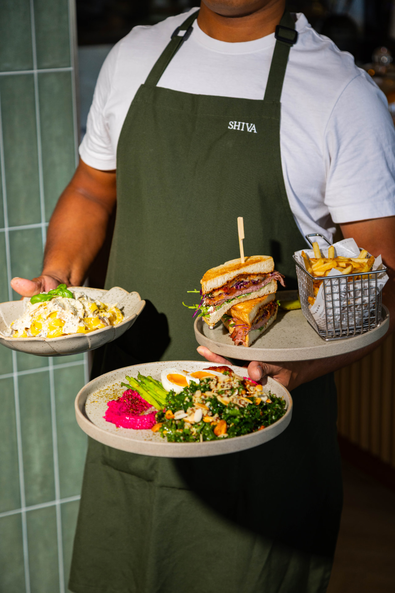 Tavia server carrying pasta, a club sandwich with fries and a kale quinoa salad